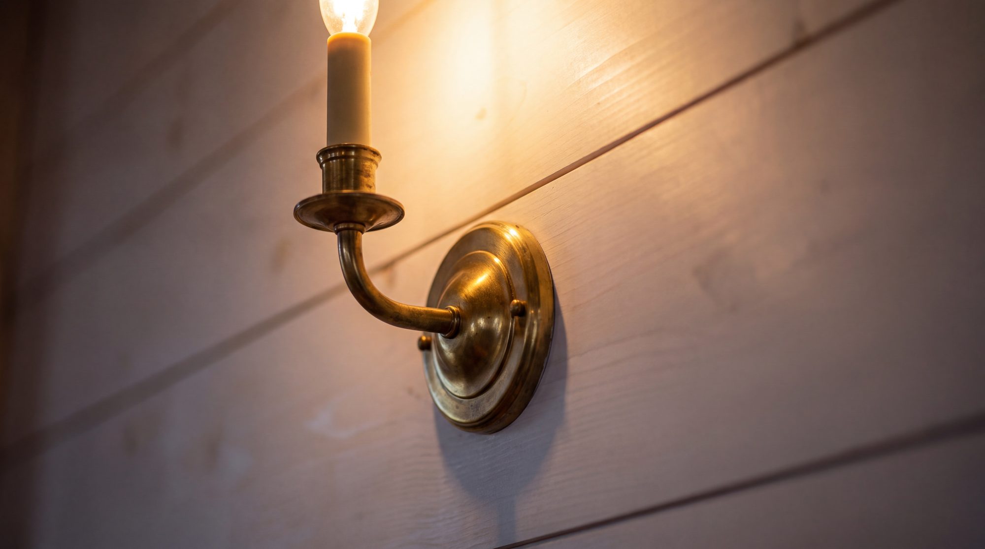 A lit brass sconce on white shiplap